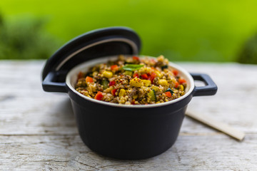 Millet groats with ground beef and vegetables and herbs in a pot on a wooden table. 