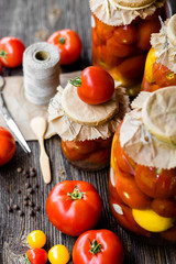 Tomato preserves in the jars, raw tomato fruits and seasonings on the wooden dark background