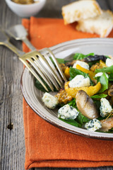Warm autumn salad with potatoes, mushrooms, bacon, spinach, mustard sauce and cheese on orange napkin. Wooden old background. Selective focus.