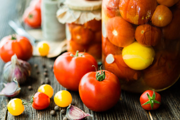 Tomato preserves in the jars, raw tomato fruits and seasonings on the wooden dark background