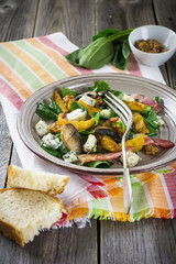 Warm autumn salad with potatoes, mushrooms, bacon, spinach, mustard sauce and cheese on orange napkin. Wooden old background. Selective focus.