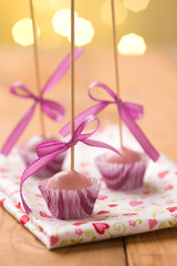 Pink Christmas cake pops sticking upside down in miniature cupcake liners. Very shallow depth of field with Christmas lights in the background