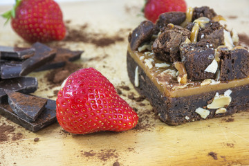 Piece of brownie with chocolate and strawberries on the light wooden background