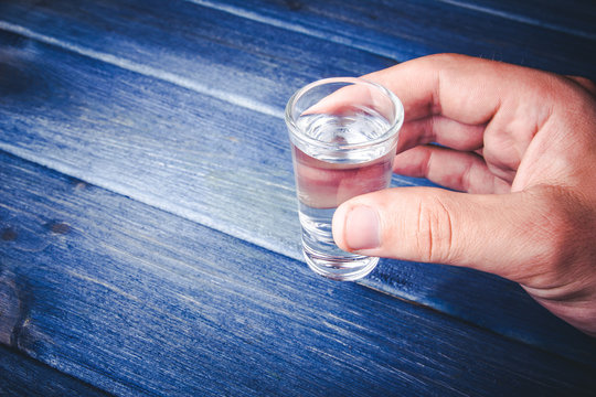 Hand Over Blue Wooden Table Holding Glass Vodka Shot.