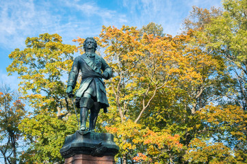 Fototapeta na wymiar Monument to Peter the Great in Kronstadt town, Leningrad region, Russia. Autumn yellow leaves background
