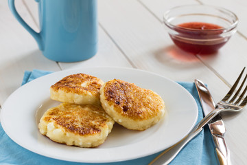 Pancakes of cottage cheese with a sweet sauce on a white table.