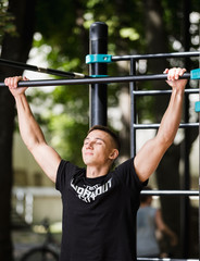 Young man doing pull ups on horizontal bar outdoors, workout, sport concept
