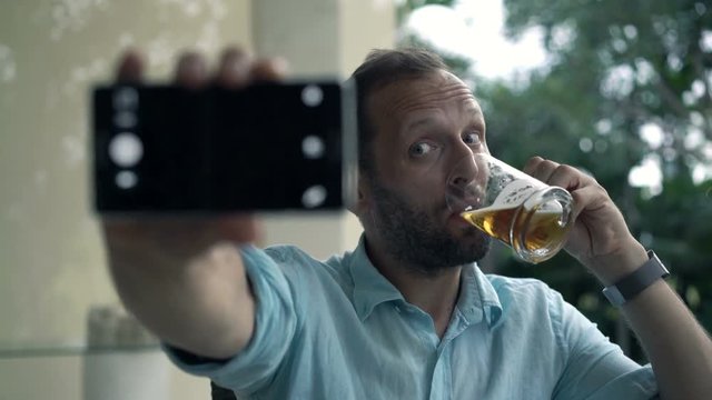 Young man with beer taking selfie photo with cellphone in the garden, 4K
