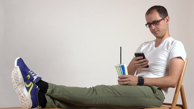 Man in black rim glasses holding plastic cup and using his mobile phone. Leisure time. Blanc space for adding your graphics or inscriptions. 4K shot