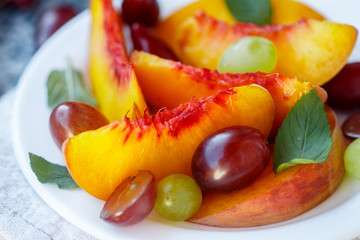 Fruit salad in white plate. Snack of fresh peaches, grapes  and mint leaves. Healthy Breakfast. Selective focus
