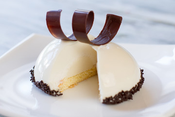 Sliced dessert on a plate. Icing of white color. Mousse cake and chocolate spiral. Cream with vanilla taste.