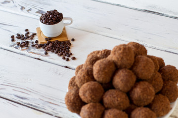 Sweets and coffee beans. White cup on wooden background. Freshly cooked rum balls. Lots of sugar and caffeine.