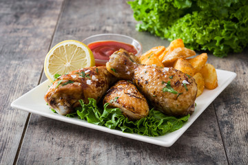 Roast chicken drumsticks and chips on wooden table

