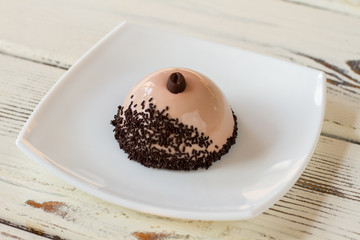 Dome shaped dessert on plate. Dish with mirror icing. Coffee mousse cake with decoration. Plain design and good taste.