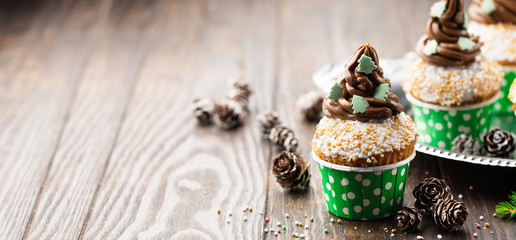 Christmas vanilla Cupcakes with chocolate buttercream icing and holiday decorations on the rustic...