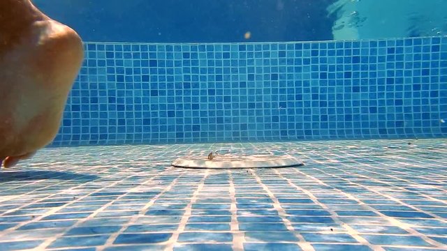 A male feet walking in a swimming pool with a white strainer in background (underwater).