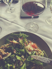 Salad on a plate with bacon, parmesan, greens and tomatoes and a glass of red wine