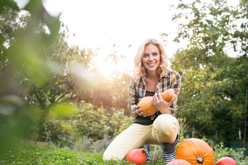 Beautiful young blond woman in her garden harvesting pumpkins