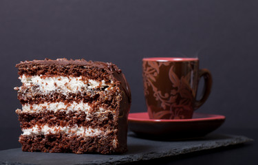 Piece of chocolate cake and cup of coffee on slate plate on blac