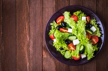 Greek salad (lettuce, tomatoes, feta cheese, cucumbers, black olives) on dark wooden background top view. Space for text. Healthy food.