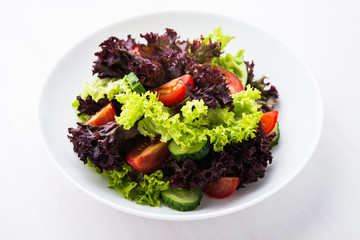 Fresh salad with green and purple lettuce, tomatoes and cucumbers on white wooden background close up. Healthy food.