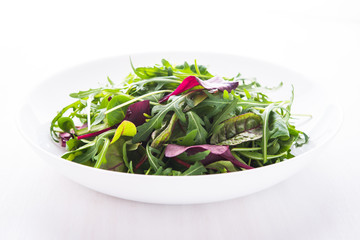 Fresh salad with mixed greens (arugula, mesclun, mache) on white wooden background close up. Healthy food.