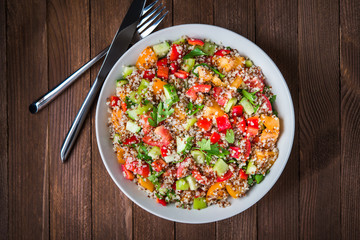 Fresh healthy salad with quinoa, colorful tomatoes, sweet pepper, cucumber and parsley on wooden background top view. Food and health. Superfood.