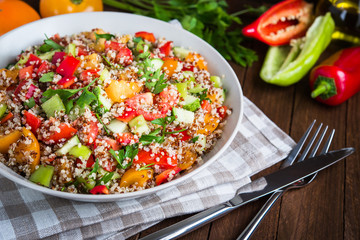Fresh healthy salad with quinoa, colorful tomatoes, sweet pepper, cucumber and parsley on wooden background close up. Food and health. Superfood.