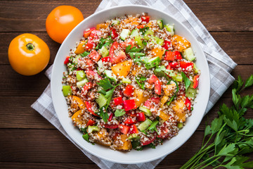 Fresh healthy salad with quinoa, colorful tomatoes, sweet pepper, cucumber and parsley on wooden background top view. Food and health. Superfood.
