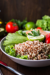 Healthy salad bowl with quinoa, tomatoes, chicken, avocado, lime and mixed greens (lettuce, parsley) on wooden background close up. Food and health.
