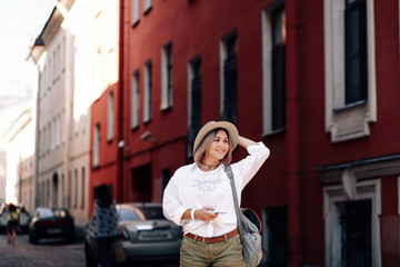 Fototapeta na wymiar Young pretty hipster cheerful girl posing on the street at sunny day, having fun alone, stylish vintage clothes hat. Travel concept