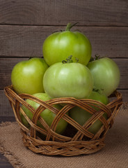 unripe green tomatoes in a wicker basket on wooden table with sacking