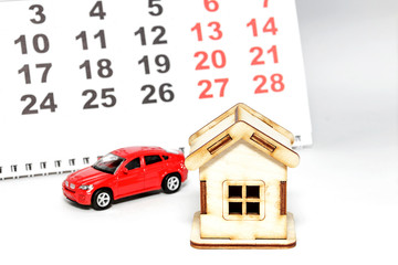 Wooden house and toy car on a calendar background