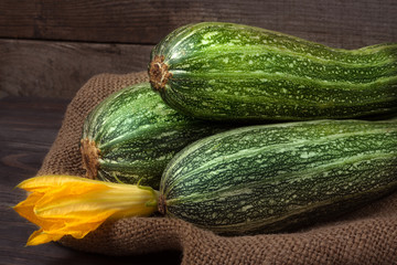 two zucchini on sackcloth and wooden background with flower