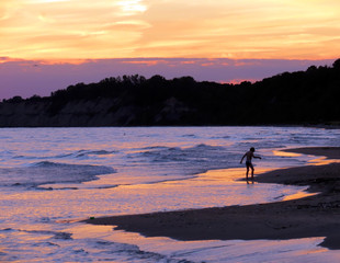 A young boy playing on the beach at sunset.