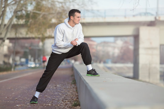 Shot of a young man exercising outdoors. He is doing stretching exercise for his legs and looking away.