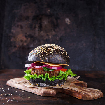 Beef burger with a black bun,with lettuce and mayonnaise and ketchup served on pieces of brown paper on a rustic wooden table of counter, on a dark background.selective focus