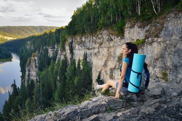 Young woman hiker with backpack sitting on edge of cliff at high altitude