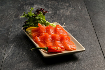 Red fish on a white plate with lettuce leaves on a dark stone background