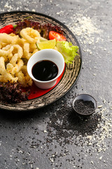 Traditional Japanese food, fried squid rings in batter with soy sauce, vegetables and red pepper on plate dark
