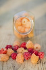 Multicolored raspberries in a glass jar on  old wooden background