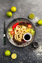 Traditional Japanese food, fried squid rings in batter with soy sauce, vegetables and red pepper on...