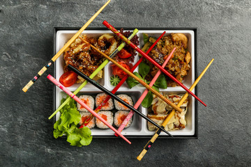 Traditional Japanese Bento lunch business. As part of the rice, sushi, vegetables, fish. Packaging is on a black background, next to chopsticks.
