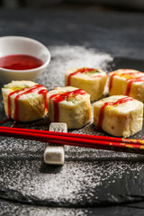 Sweet sushi with red strawberry jam on a black plate