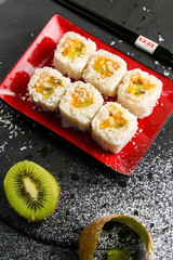 Traditional Japanese sushi with sweet fruit on black plate, next lie oranges and kiwi