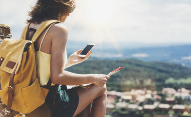 Hipster young girl with bright backpack looking at phone and map. Said view tourist traveler on background mountain, blue sea, sun flare. Mockup for text message. Female hands using smartphone