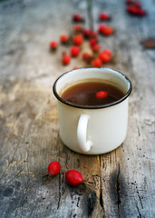 Tea in an iron mug and red  rosehip on an old wooden surface of a table
