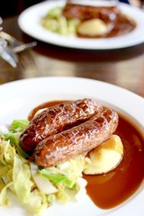 Sausage and mashed potato with seasonal greens served with red wine gravy on a white plate
