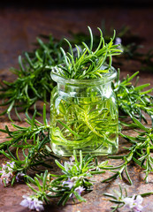 Rosemary essential oil jar and plant with flowers, rustic background