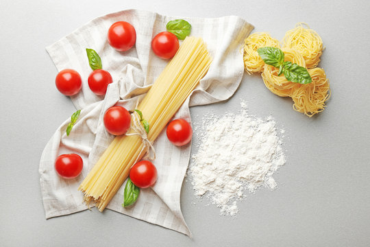 Different dry pasta with cherry tomatoes on table